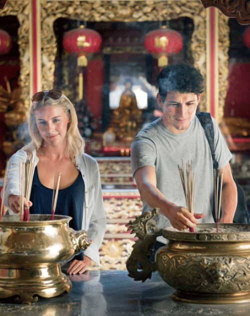 Couple lighting incense at a temple during a cultural honeymoon tour in Asia, symbolizing romance and spiritual connection.