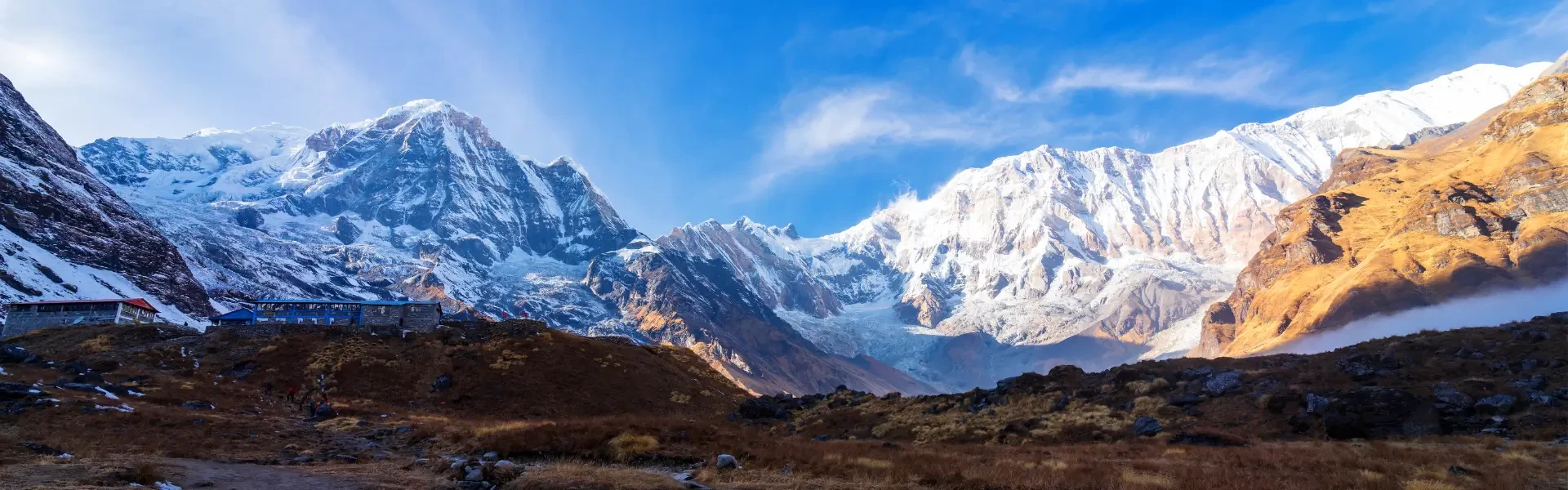 anoramic view of the Annapurna mountain range in the Nepal Himalayas, featuring snow-covered peaks like Annapurna South and Machhapuchhre (Fishtail Mountain), set against a blue sky.