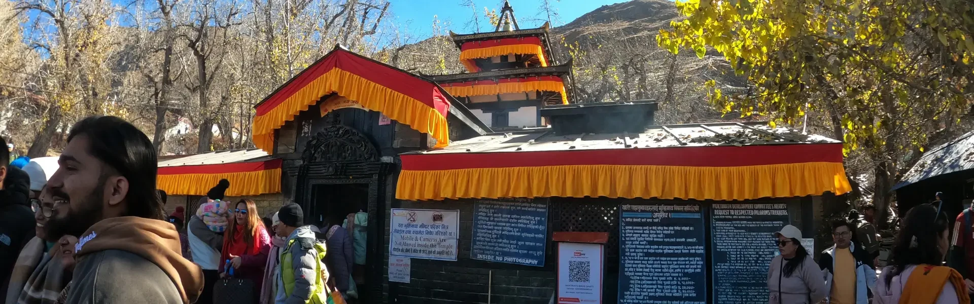 Muktinath Temple in the Mustang region of Nepal, showing the pagoda-style temple structure, the 108 waterspouts, and prayer flags against the backdrop of the Himalayan mountains.
