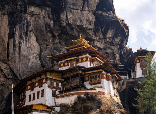 The iconic Tiger's Nest Monastery (Paro Taktsang) clinging precariously to a cliffside high above the Paro Valley in Bhutan, surrounded by green mountains.